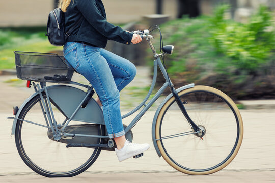 Woman wear jeans denim cycling vintage bicycle on European city street dynamic motion blurred background on sunny day. Urban bike commute work ride employee healthy lifestyle eco-friendly transport - Powered by Adobe