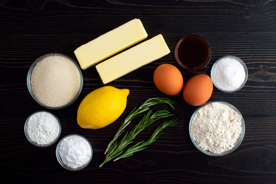 Rosemary-Lemon Sugar Cookies Ingredients: Flour, butter, sugar, eggs, and other cookie ingredients on a dark wooden table