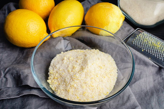 Homemade Lemon Sugar in a Glass Bowl: Sugar mixed with grated lemon peel lemon zest with fresh lemons in the background