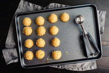 Scoops of Sugar Cookie Dough on a Sheet Pan: Directly above a non-stick baking pan with balls of cookie dough and a cookie scoop
