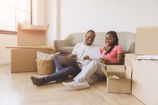 Happy African American Couple Organizing Move Using Laptop and Documents - Powered by Adobe