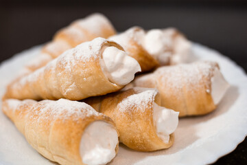 Fragrant puff pastry tubes with protein cream on a white plate. Preparation of sweet pastries, close-up