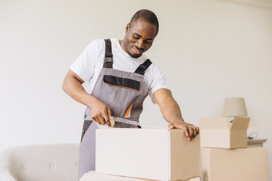 African American mover packing boxes using packing tape dispenser during house move