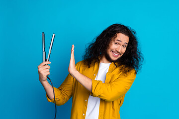Young man with curly hair and beard gesturing humorously while refusing a hair styling tool in a...
