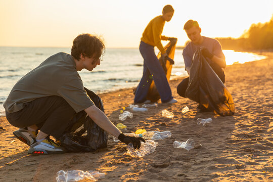 Earth day. Volunteers activists team collects garbage cleaning of beach coastal zone. Woman mans puts plastic trash in garbage bag on ocean shore. Environmental conservation coastal zone cleaning