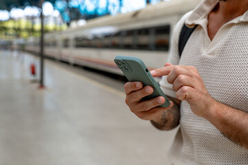 Tourist checking a smartphone app on the train station platform, waiting for the train's arrival and planning the next journey
