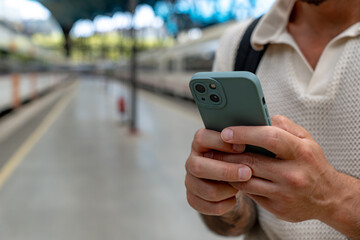 Close-up of a tourist holding a smartphone at a train station, waiting for departure while checking schedules and travel information