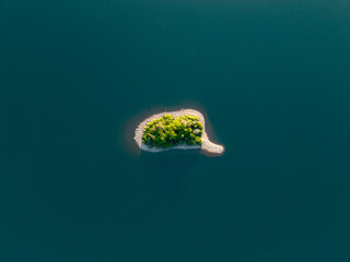 Aerial top down view of a small paradise island with trees surrounded by water