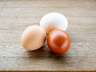 Three Easter eggs in various colors resting on a rustic wooden table.