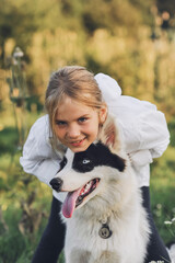 Little blond girl hugging her pet dog outdooors on nature in summer. Yakutian Laika dog breed. Happy childhood concept