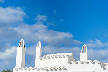 Whitewashed Mediterranean rooftop with traditional chimneys against a bright blue sky. Classic...