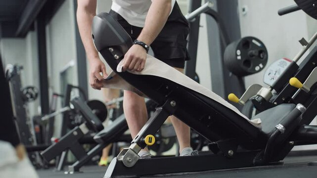 Keep fit buff spreads sports towel on weight bench then seats comfortably on machine preparing for leg press with controlled posture under modern gym lighting capturing post workout readiness focus