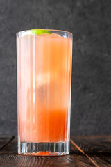 Guava Collins cocktail sparkles in tall glass with lime against dark backdrop