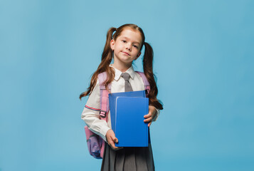 Little brunette schoolgirl holding books on blue background.