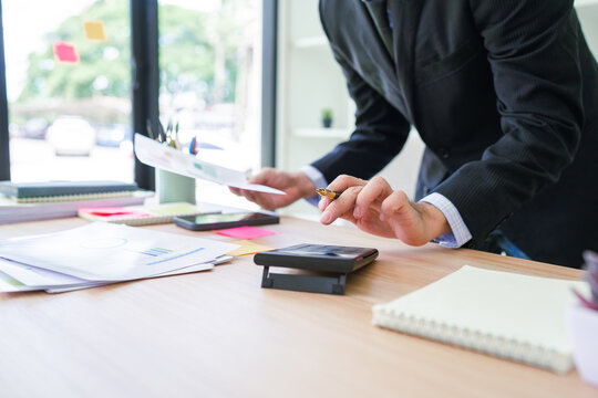 Asian businessman pressing button on calculator and calculate about analysis with looking data on tablet screen.