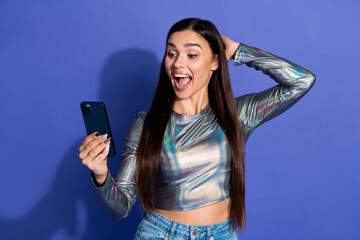 Excited young woman reading something surprising on her smartphone against a stylish violet background