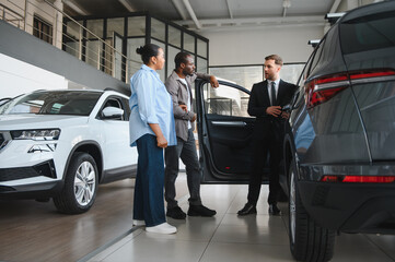 Car salesman showing new vehicle to african american couple in dealership