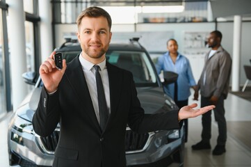 Fototapeta premium Car salesman holding keys presenting new vehicle to african american couple