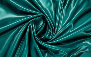 Close-up of a teal-colored, glossy fabric arranged in a swirling, twisted pattern. The material reflects light, creating highlights and shadows across its smooth, flowing surface.