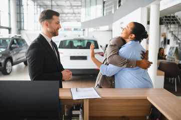 Happy African american couple hugging at car dealership after buying new vehicle