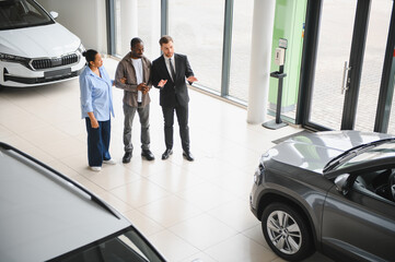 Car salesman showing new vehicle to african american couple in dealership