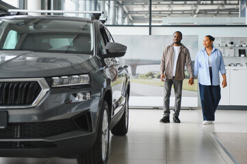 Happy couple holding hands choosing new car in dealership showroom