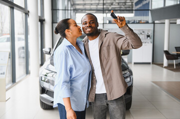 Happy african american couple showing new car key in dealership showroom