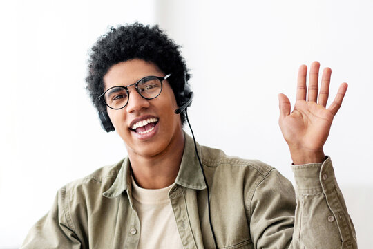 Web-based communication concept. Black teen guy talking to his college tutor on laptop computer from home. Positive African American youth waving to his fellow students during online video conference