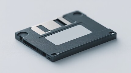 single black floppy disk lies on white surface casting gentle shadow against pale background with ample copy space