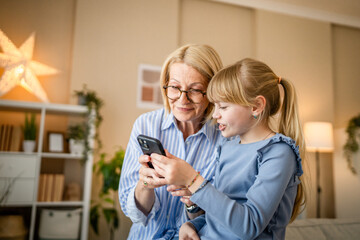 Fototapeta premium grandma and granddaughter use mobile phone together in the living room