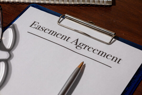 A legal easement agreement rests beside a judge&rsquo;s gavel on a wooden desk, symbolizing land rights, property access, and legal boundary arrangements.