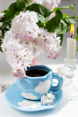 a cup with clouds on a blue background with tea. A strong hot drink for breakfast, a bouquet of lilacs in a vase