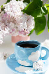 a cup with clouds on a blue background with tea. A strong hot drink for breakfast, a bouquet of lilacs in a vase