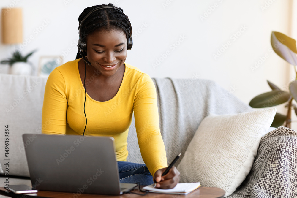 Aufkleber Online Education Concept. Smiling Black Woman In Headset Studying With Laptop At Home And Taking Notes To Notepad, Enjoying Distance Learning, Watching Webinar In Internet And Noting Highlights