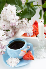 a cup with clouds on a blue background with tea. A strong hot drink for breakfast, a bouquet of lilacs in a vase