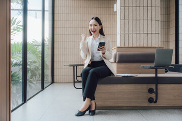 Fototapeta premium Excited Asian Businesswoman Celebrating Success with Phone