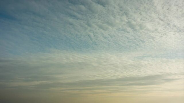 Overcast day showing altocumulus clouds stretching across a light blue atmosphere above the horizon, calm sky background.