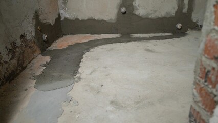 Construction workers carefully pouring wet concrete floor screed, leveling surface with precision for new bathroom renovation project, ensuring smooth, even foundation