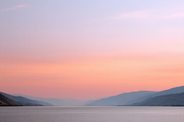 serene summer sunset over tranquil lake with soft hues of orange and pink reflecting on water
