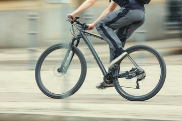 Man in sport suit riding fast black bicycle on European city street dynamic motion blurred background on sunny day. Urban bike commute work ride employee healthy lifestyle eco-friendly transport