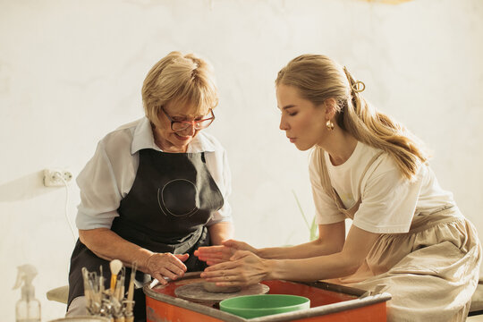 Senior woman learning pottery with young instructor