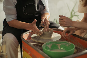 Senior potter teaching apprentice clay throwing technique on pottery wheel