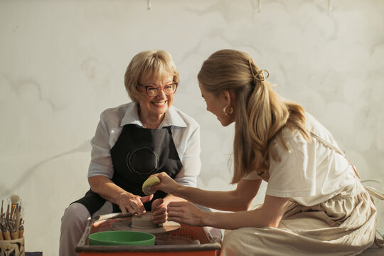 Senior woman learning pottery with young instructor creating clay vase