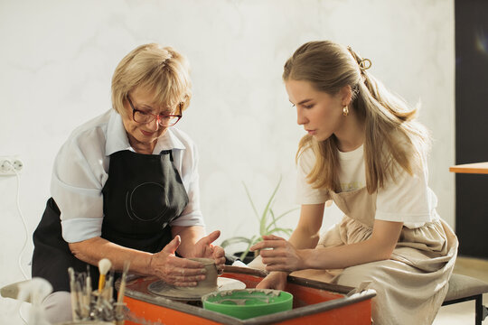 Senior woman learning pottery making with young instructor