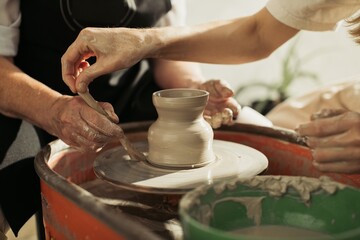 Potter working on a clay vase on a pottery wheel with wooden tool