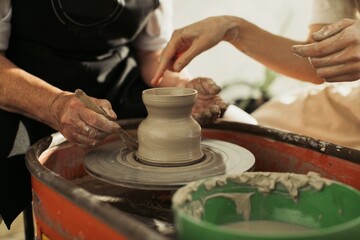 Potter using wooden tool shaping clay on pottery wheel with apprentice