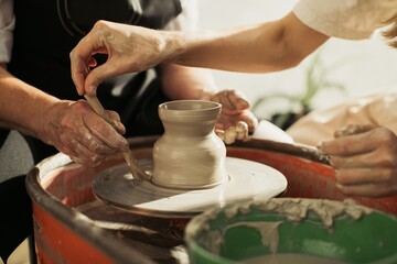Potter teaching student how to mold clay on pottery wheel