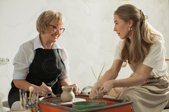Senior woman learning pottery with young instructor