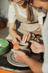 Potter creating a clay pot with apprentice on pottery wheel