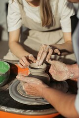 Potter teaching apprentice shaping clay on pottery wheel